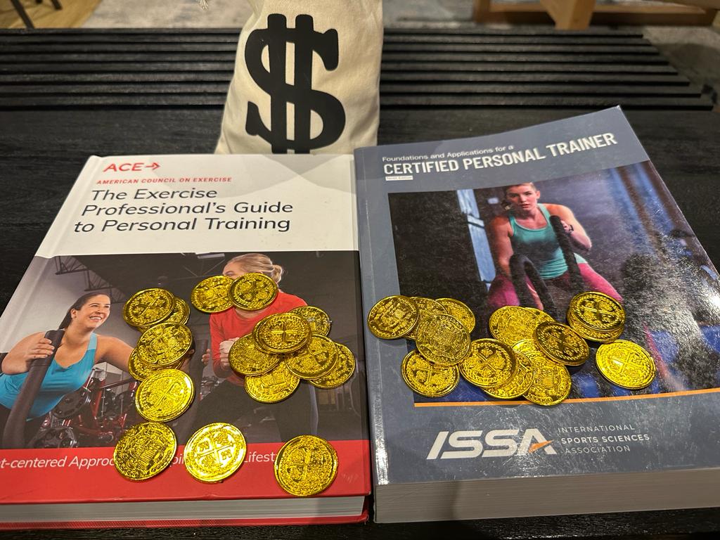 ACE and ISSA textbooks on a table with a money sign behind them and gold coins - Ace vs ISSA, which certification costs more