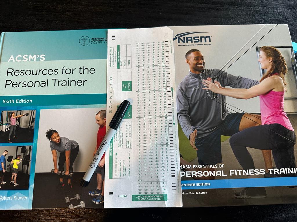 ACSM vs NASM - textbooks for ACSM and NASM on table with exam scantron sheet between them with a sharpie - which test is harder