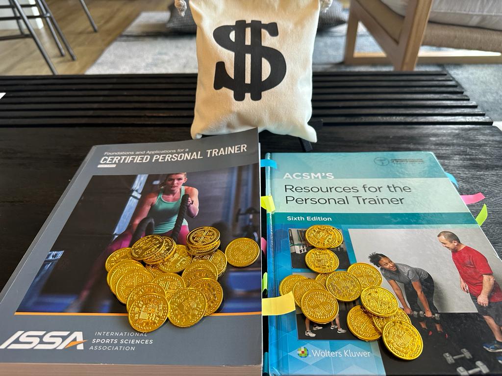 ACSM vs ISSA - ISSA and ACSM textbooks on a table with gold coins and a bag with a money sign - which is more costly