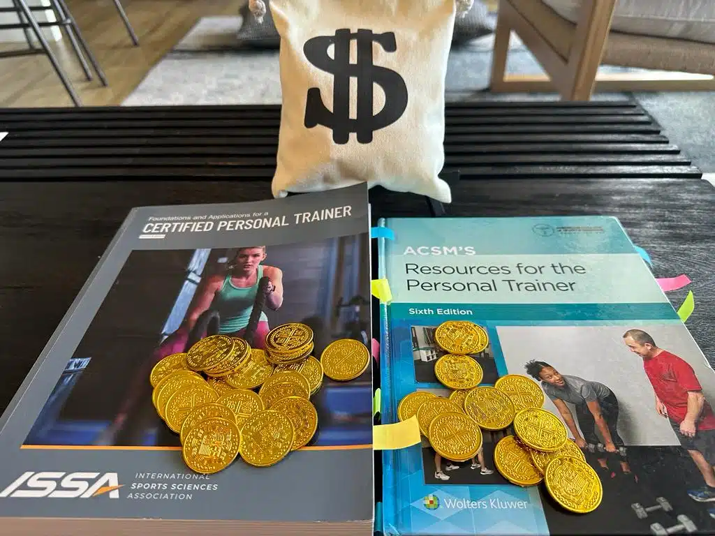 ISSA vs ACSM - Which Fitness Certification is Best? 42 ACSM vs ISSA - ISSA and ACSM textbooks on a table with gold coins and a bag with a money sign - which is more costly