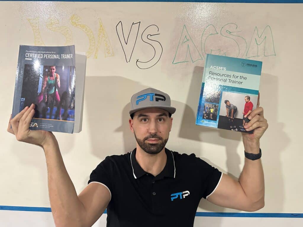 Tyler Read holds up ACSM and ISSA textbooks against a whiteboard saying ISSA vs ACSM