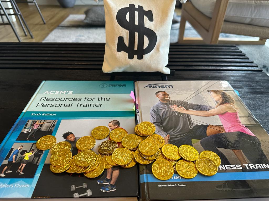 NASM vs ACSM - ACSM and NASM textbooks laid out on table with gold coins and money bag 