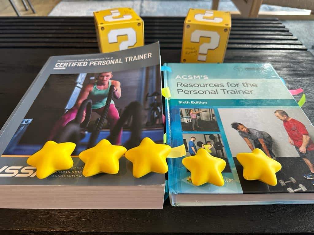 ISSA and ACSM textbooks on table with gold stars and yellow question boxes