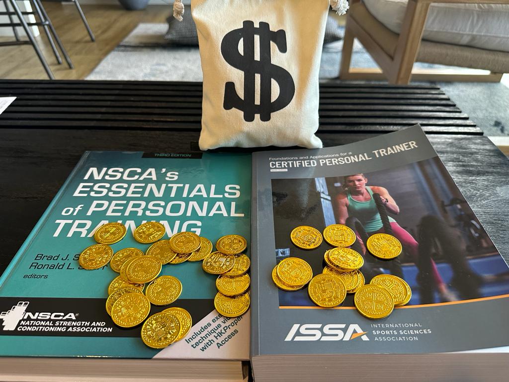 NSCA and ISSA textbooks on table with gold coins on them and a money bag - which personal trainer certification costs more