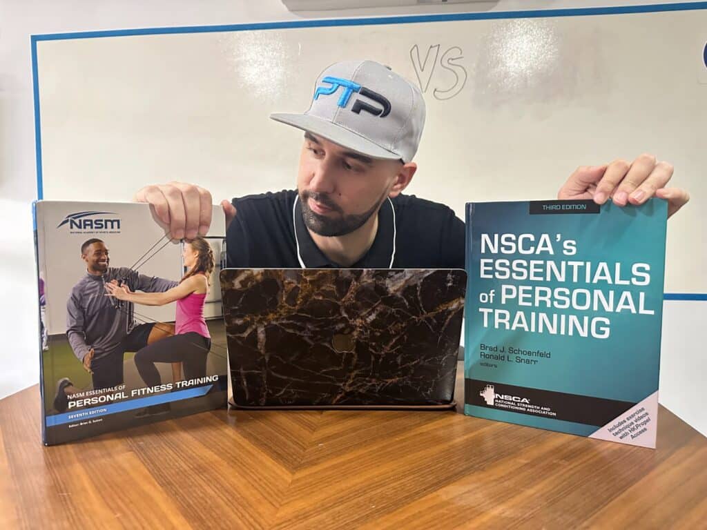 NASM vs NSCA - Tyler Read holds up NSCA and NASM textbooks on a table with a laptop in front of a whiteboard 