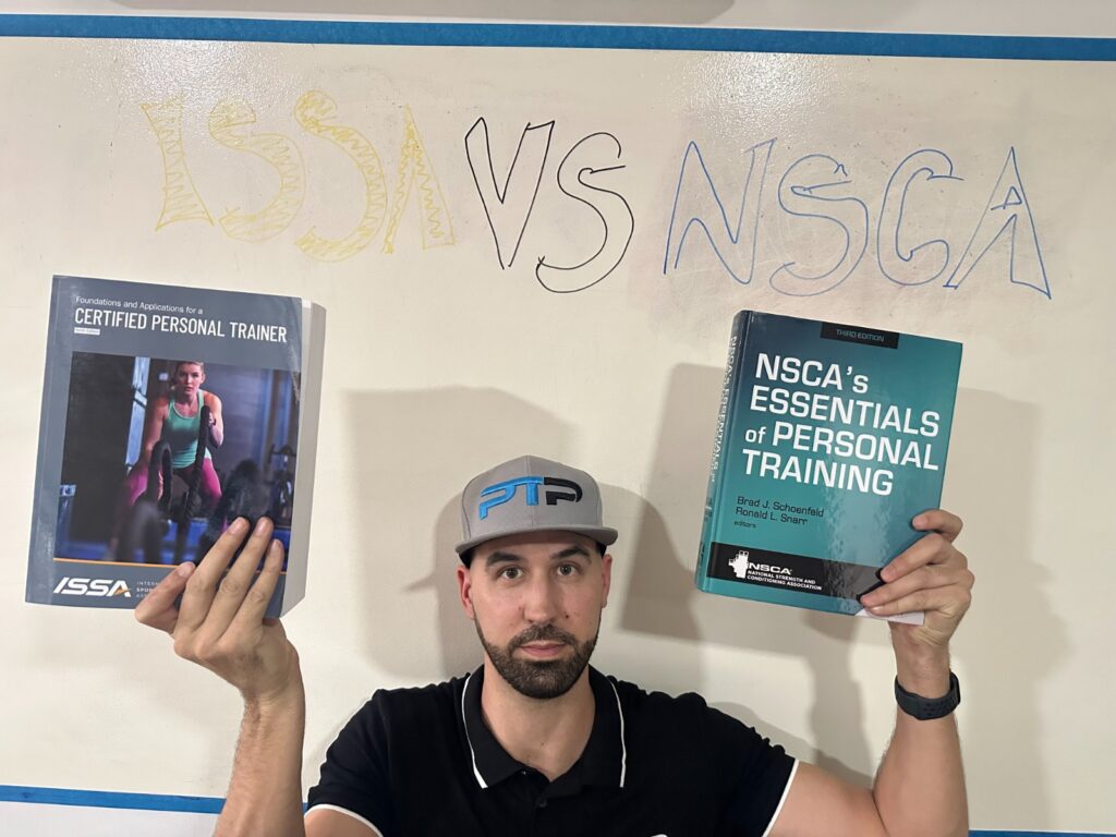 NSCA vs ISSA - Tyler read holds up ISSA and NSCA textbooks in front of white board with ISSA vs NSCA on it