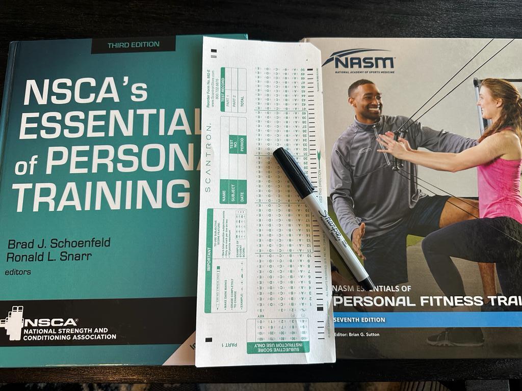 NSCA vs NASM - NSCA and NASM textbooks on table with scantron exam sheet in between them with a sharpie pen