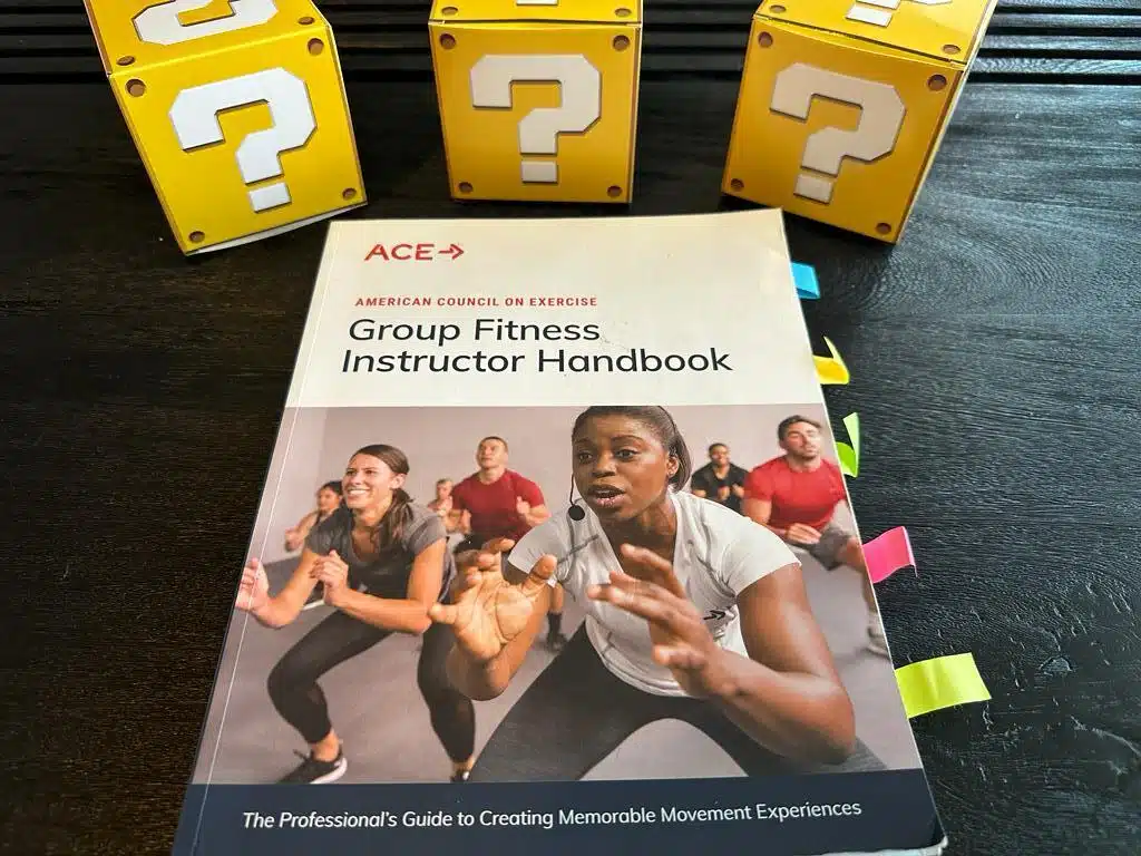best group fitness instructor certifications - ace handbook on desk with yellow question mark boxes