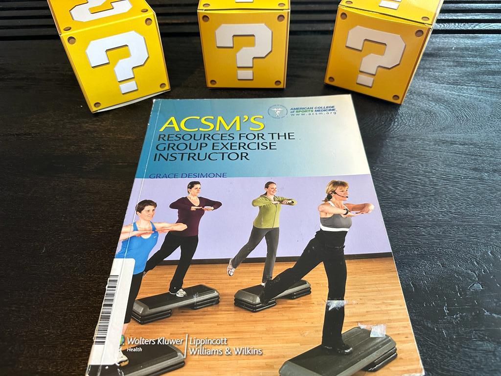 best exercise instructor certification - acsm group exercise textbook on table with yellow question mark boxes