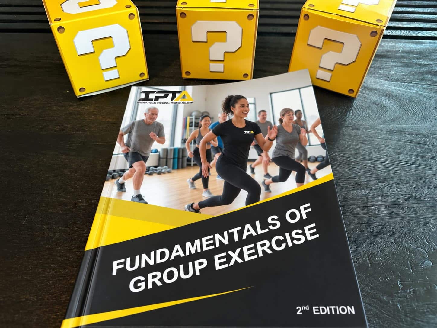 How to pick the best group fitness certification (Updated) 30 best group exercise certifications - IPTA group exercise specialist textbook on table with yellow question mark boxes