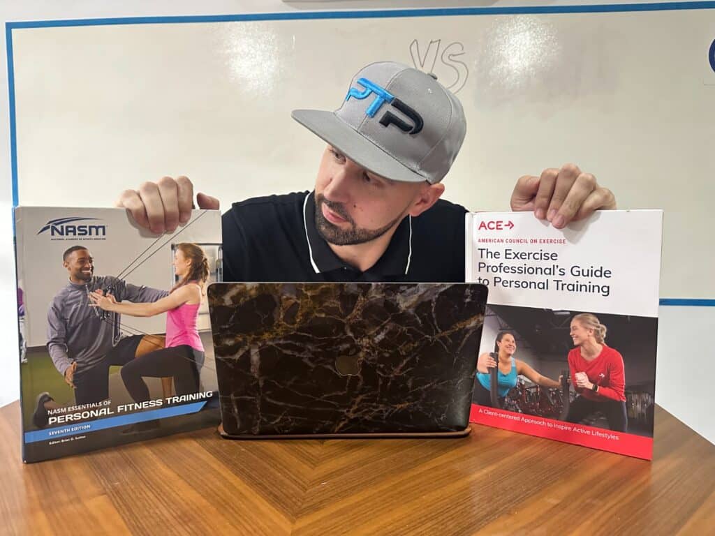 ACE vs NASM - Tyler holds up both NASM and ACE textbooks on a desk in front of white board - which is better