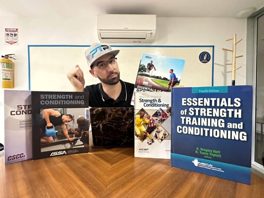 5 best strength and conditioning certifications - Tyler Read sits at a table with the various strength and conditioning certification textbooks