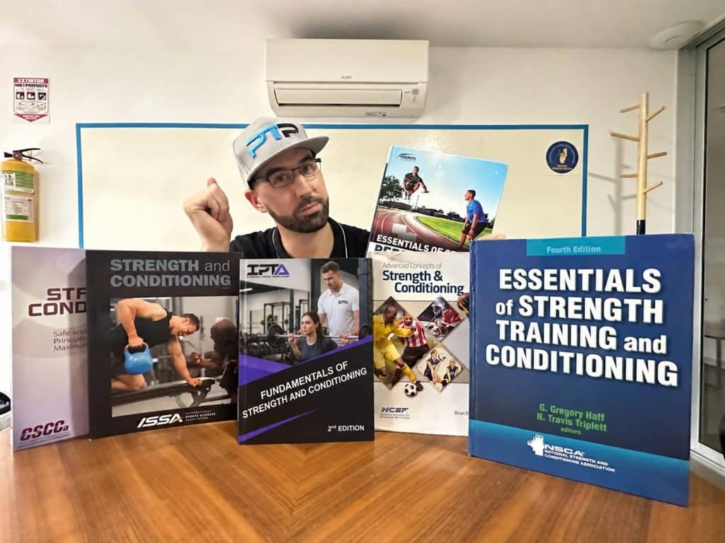 5 best strength and conditioning certifications - Tyler Read sits at a table with the various strength and conditioning certification textbooks