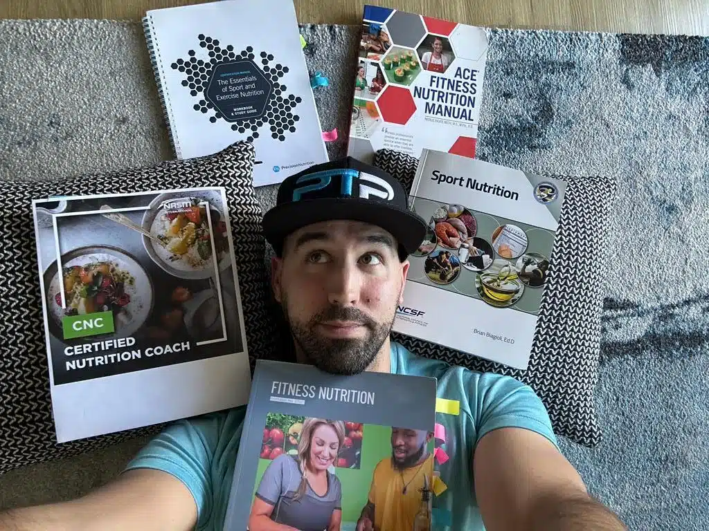 Best Nutrition Certifications- Tyler Read laying on the floor surrounded by the top nutrition certifications textbooks, ACE, NASM, NCSF, Precision Nutrition, ISSA
