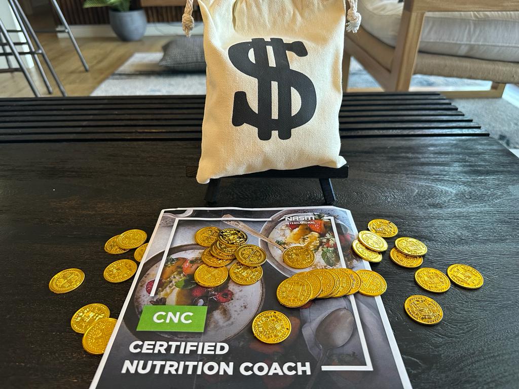 NASM Nutrition coach cost and course options - NASM CNC textbook with gold coins on table.