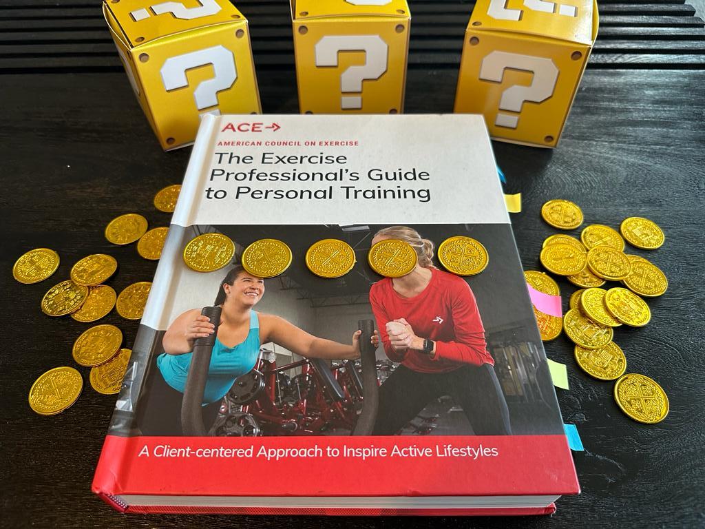 Cheapest personal training certifications - ACE textbook laid out on table with gold coins and mystery boxes - how much does ACE CPT cost?