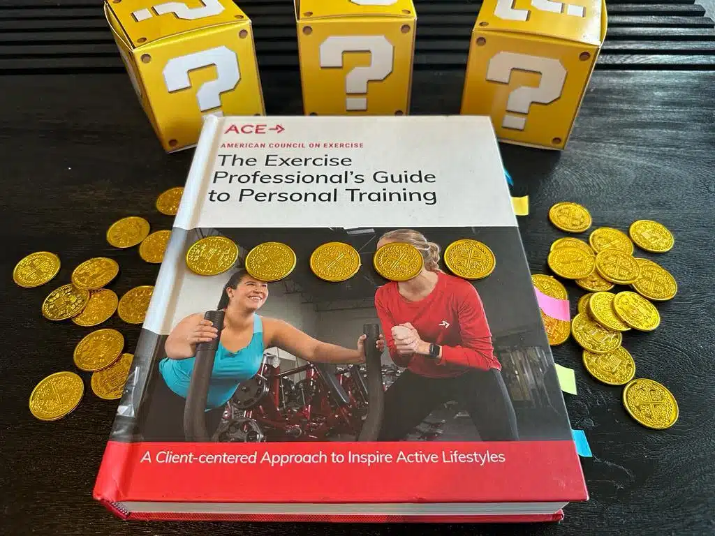 The 9 Cheapest Personal Training Certifications 12 Cheapest personal training certifications - ACE textbook laid out on table with gold coins and mystery boxes - how much does ACE CPT cost?