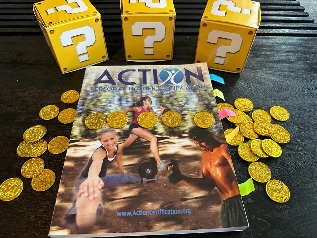 cheapest personal training certification - ACTION textbook laid out on table with gold coins and mystery boxes - how much does ACTION CPT cost?