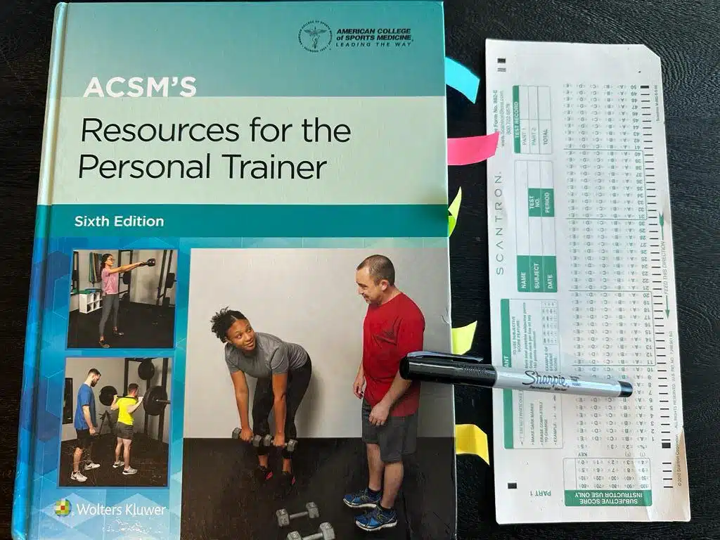 Easiest training certifications - ACSM CPT textbook laid out with a copy of scantron exam next to it and a sharpie 