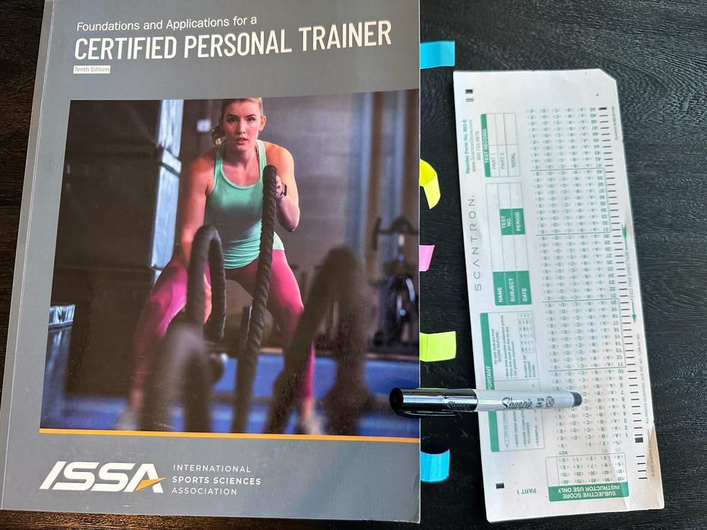 Easiest personal training certifications - ISSA CPT textbook laid out with a copy of scantron exam next to it and a sharpie 