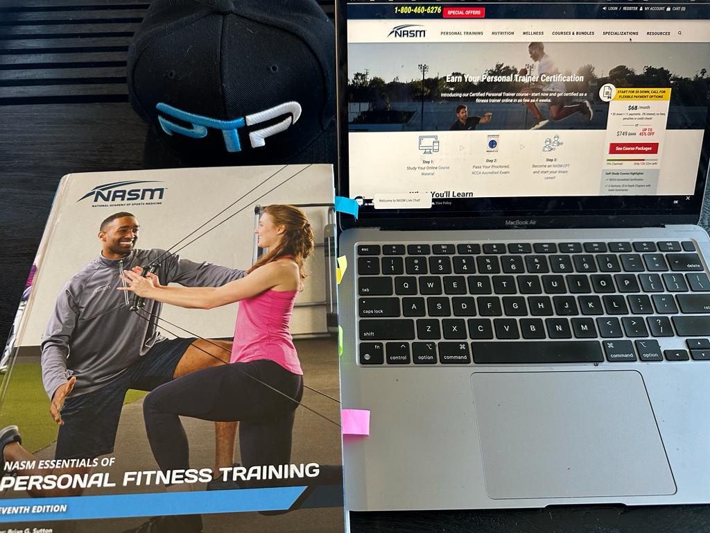 best online training certifications - NASM textbook on table next to ptpioneer hat and laptop displaying nasm website - should you pick nasm