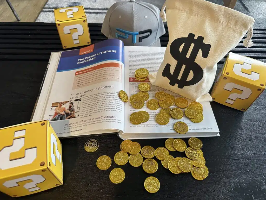 NASM Certification Review 2023 - Is NASM Legit? 41 NASM Certification Cost and Packages - NASM textbook with gold coins displayed on table