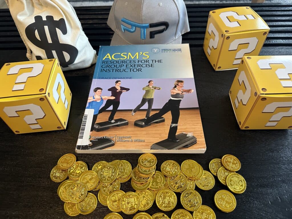 acsm group instructor cost. acsm group exercise textbook with gold coins on table.