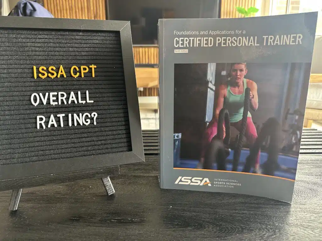 ISSA Training Certification Review 2023 - Is ISSA Worth It? 22 ISSA CPT program overall rating - ISSA trainer textbook on table with ISSA overall rating displayed