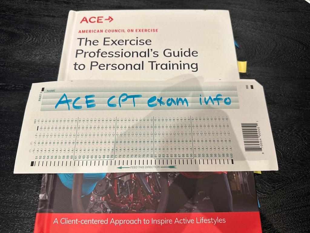 ACE personal trainer textbook on table with ACE exam info for preparation for the CPT exam.