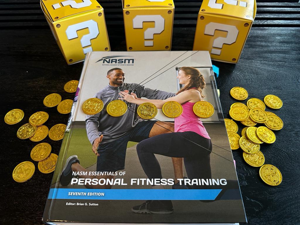 Cheapest personal training certification - NASM CPT. NASM personal trainer textbook displayed on table with gold coins.