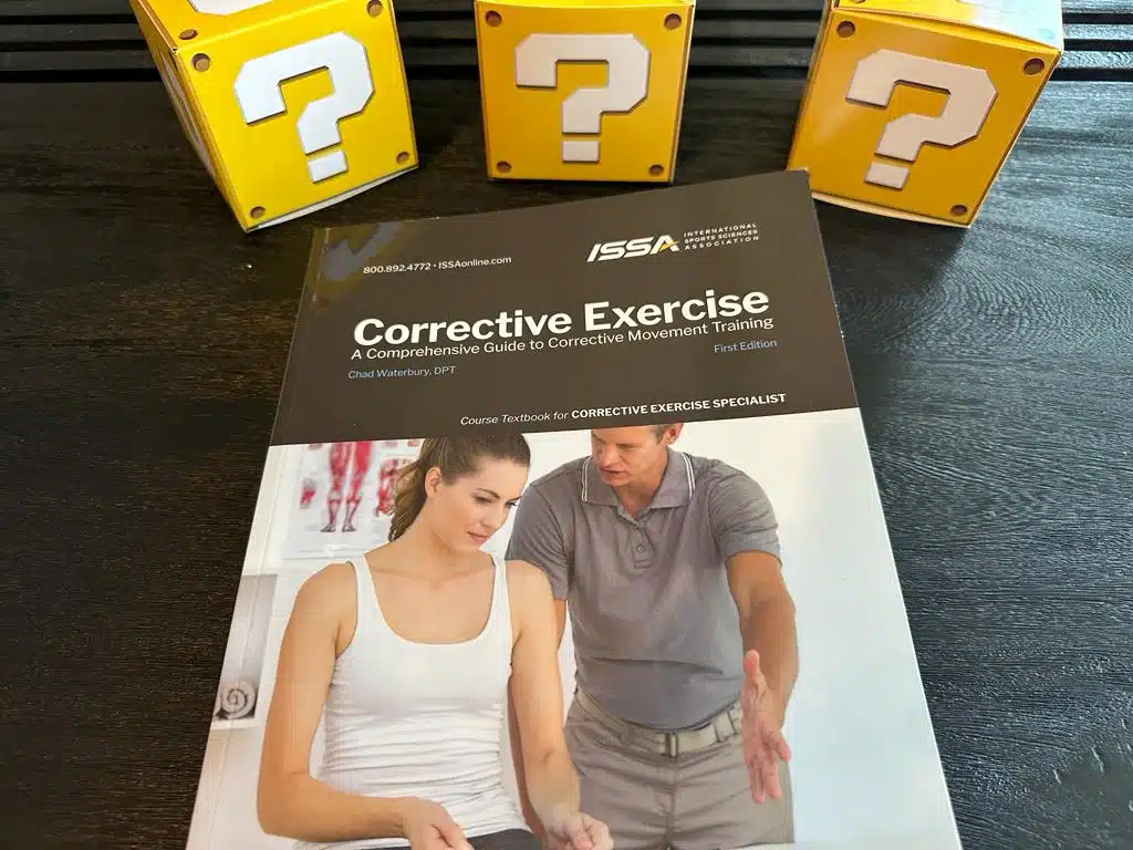 Best Corrective Exercise Training Program (ISSA vs NASM vs TBMM) 7 best corrective exercise certification - ISSA corrective exercise textbook laid on table with question boxes