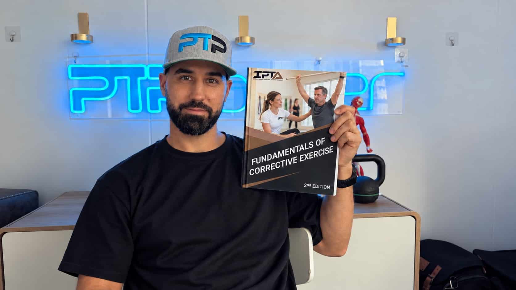 Tyler holds the Corrective Exercise Specialist textbook for IPTA.